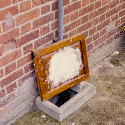 The image features a brick wall with a wooden frame and glass window mounted on it. The window is placed in the middle of the wall, creating an interesting focal point. A concrete block can be seen next to the wall, adding texture and depth to the scene.