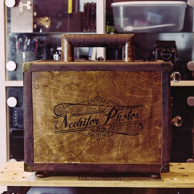The image features a wooden suitcase with the word "Niechter" written on it. It is placed on top of a table, which appears to be made from wood as well. The suitcase has a vintage look and seems to be an old-fashioned piece of luggage.