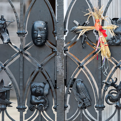 The image features a black metal gate with various decorations on it. There are several bird statues attached to the gate, as well as other ornaments and figurines. Some of these decorations include a face carved into one of the gates, adding an artistic touch to the overall appearance.