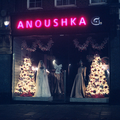 The image features a storefront with a large window display showcasing wedding dresses. There are several mannequins dressed in elegant gowns, each wearing different styles of bridal attire. The store is called Anoushka and has an inviting atmosphere for potential customers.