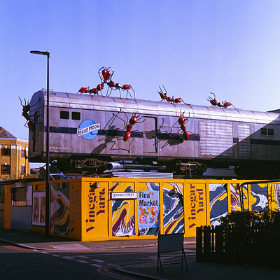 The image features a train with Santa Claus and reindeer on top of it, traveling down the tracks. There are several people standing around the train, possibly admiring or waiting for it to pass by. In addition to the train, there is a car parked in the background, as well as two traffic lights visible near the right side of the image.