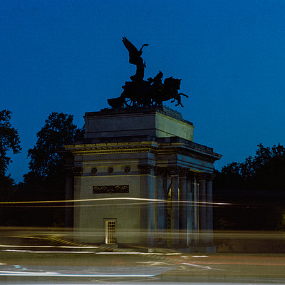 The image is a black and white photo of a large building, possibly a monument or a government building. In the foreground, there are blurry lights that create an interesting effect on the scene. A statue of a bird can be seen atop the building, adding to its grandeur.
