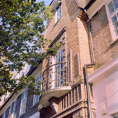 The image features a large brick building with many windows. There are two prominent windows on the side of the building, one near the top and another at the bottom. Above these windows is an iron balcony or railing that adds to the architectural charm of the building.