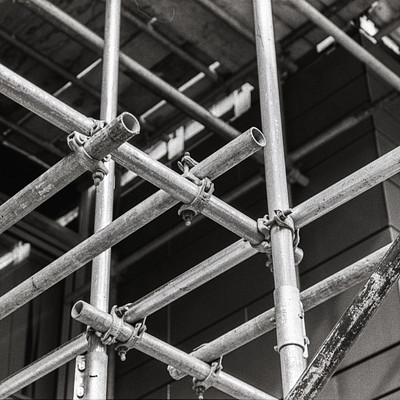 The image is a black and white photo of a building under construction. There are several sets of scaffolding surrounding the building, with some of them being taller than others. These scaffoldings provide support to workers during the construction process.