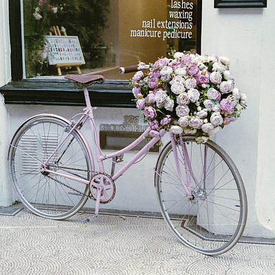 The image features a pink bicycle parked outside of a building. It is adorned with a beautiful bouquet of flowers, creating an eye-catching display. The bike is positioned next to the storefront window, drawing attention to it and possibly indicating that it's for sale or rent.