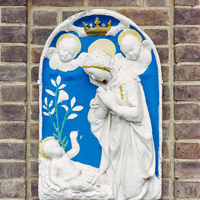 The image features a beautifully crafted blue and white stained glass window, depicting an angelic scene. In the center of the window, there is a statue of Mary holding a baby Jesus. Surrounding this central figure are several other figures, including angels and possibly saints, all adorned with intricate designs.