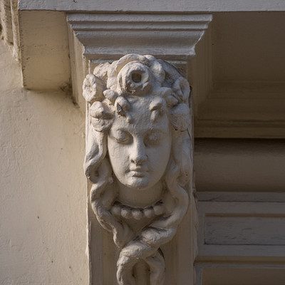 The image features a white building with an ornate design on the side of it. A statue is prominently displayed, depicting a woman's head with a crown and a snake wrapped around her neck. This intricate carving adds a touch of elegance to the building's exterior.