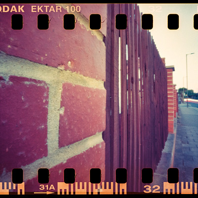 The image is a black and white photo of a brick wall with a red brick pattern. The wall appears to be part of an old building, possibly a fence or a gate. There are several bricks visible on the wall, creating a textured appearance.