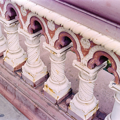 The image features a pink stone bench with an ornate design. It has several carved columns supporting the bench, giving it a fancy and elegant appearance. The columns are arranged in various positions around the bench, creating a visually appealing structure.