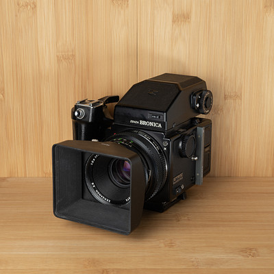 The image features a black and white vintage camera sitting on top of a wooden table. The camera is positioned in the center of the frame, with its lens facing towards the viewer. The wooden surface provides an appealing backdrop for this classic piece of photography equipment.