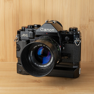 The image features a vintage Canon camera sitting on top of a wooden table. The camera is an old-fashioned model, and it appears to be in good condition. It has a large lens attached to the front, which adds to its classic appearance.
