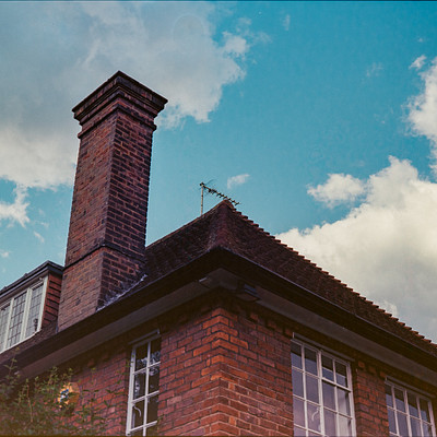 The image features a brick house with a chimney on top. The chimney is made of bricks and has a metal roof, giving it an old-fashioned appearance. Above the chimney, there are two windows in the house.