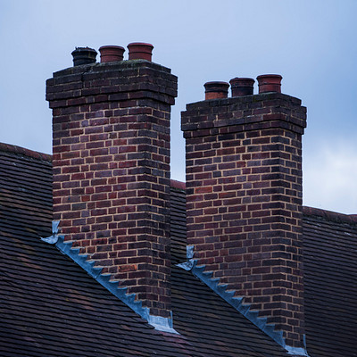 The image features a brick chimney with two red brick chimneys on top of it. These chimneys are located on the roof of a building, and they appear to be made of bricks. The sky can be seen in the background, creating a contrasting backdrop for these structures.