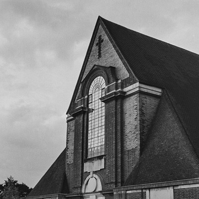 The image is a black and white photo of an old church with a steeple. The building has a brick exterior, giving it a classic appearance. A large window can be seen on the side of the building, adding to its architectural charm.