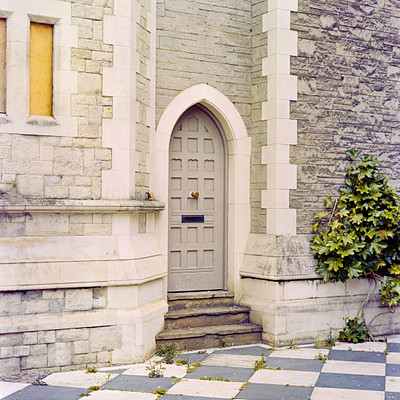 The image features a stone building with a large doorway, which is the main focus of the scene. Above the doorway, there are two windows on either side, adding to the architectural charm of the building. In front of the doorway, there is a small step leading up to it.