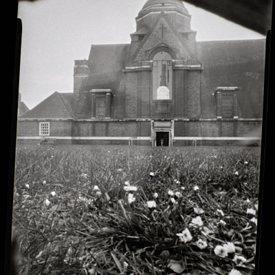 The image is a black and white photo of an old church with a steeple. The church has a brick exterior, giving it a classic appearance. There are several windows on the building, some of which have shutters.