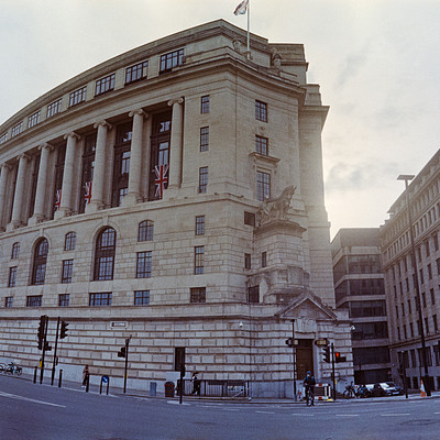 The image features a large, old building with many windows and columns. It appears to be an important or historic structure, possibly a government building or university. There are several traffic lights visible around the area, indicating that it is located in a busy urban setting.
