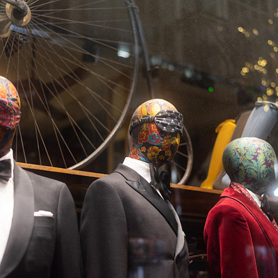 The image features a store display with three mannequins dressed in suits and ties. Each of the mannequins is wearing a different suit, showcasing various styles for potential customers to choose from. In addition to the mannequins, there are several ties visible throughout the scene, some on the mannequins and others placed separately.