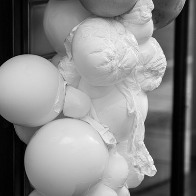 The image features a large pile of white balloons, some of which are tied together. There is an assortment of balloon sizes and shapes in the stack, creating a visually interesting display. The balloons are arranged in various positions, with some hanging from the top while others are placed on different levels within the pile.