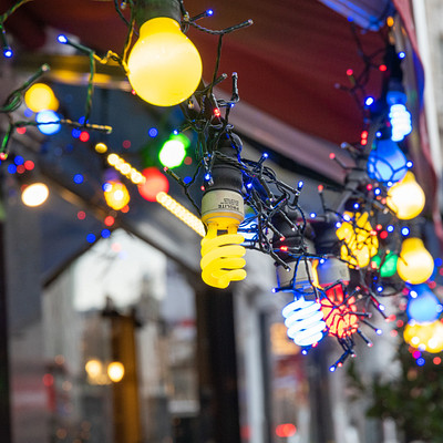 The image features a storefront with a large number of lights hanging from the ceiling. There are at least 13 lights, including some that appear to be Christmas lights, creating an eye-catching display. The lights are arranged in various patterns and colors, adding visual interest to the scene.