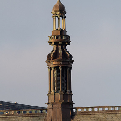 The image features a large brick building with a tall, ornate clock tower on top. The tower has a gold dome and is adorned with a cross at the very top. The clock face is visible on the side of the tower, making it an easily recognizable landmark in the area.