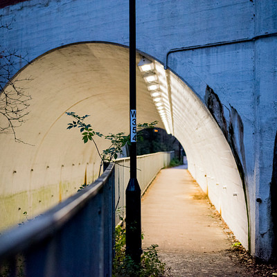 The image features a long, narrow tunnel with a sidewalk running through it. A street light is positioned at the end of the tunnel, providing illumination for pedestrians and drivers alike. The tunnel appears to be made of concrete, giving it an industrial appearance.