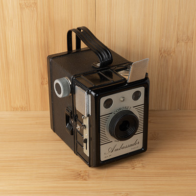 The image features a vintage camera sitting on top of a wooden table. The camera is an old-fashioned model, possibly a Kodak, and it has a leather case. It appears to be in good condition and ready for use.
