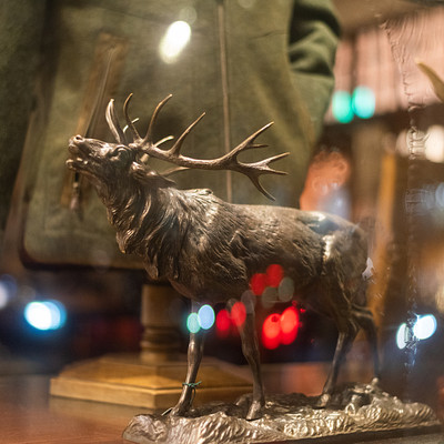 The image features a deer statue sitting on top of a table. The deer is positioned in the center of the scene, and it appears to be made of metal or bronze. In addition to the deer statue, there are several other items scattered around the room.