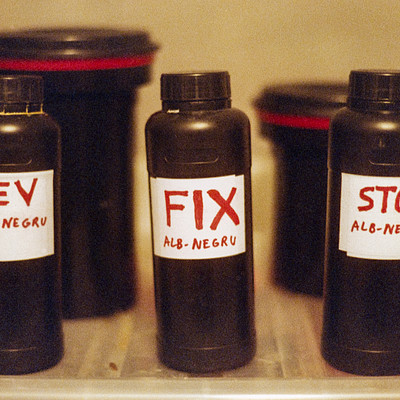 There are four bottles of different sizes and colors sitting on a table. The labels on the bottles have various words written in red marker, such as "Rev," "Fix," "Al-Negra," and "Stop." These labels suggest that these bottles might be related to some kind of repair or maintenance work.