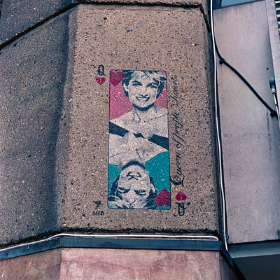 The image features a wall with a sticker of a woman's face, possibly Marilyn Monroe. The sticker is placed on the side of a building and appears to be a popular spot for people to take photos in front of it. There are several other stickers around the main one, adding more visual interest to the scene.