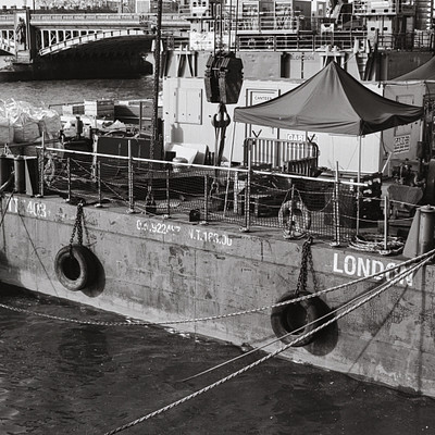 The image is a black and white photo of a large boat docked at the pier. The boat appears to be an old ship, possibly a ferry or a cargo vessel. It has several life preservers attached to it, ensuring safety for those on board.