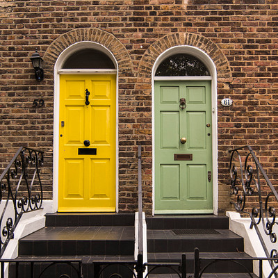 The image features a large brick building with two brightly colored doors, one yellow and the other green. These vibrant colors contrast beautifully against the red brick exterior of the house. A black metal staircase is situated in front of the building, leading up to the entrance.