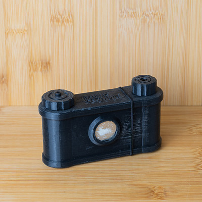 The image features a black camera with a wooden background. The camera is placed on a table, and it appears to be an old-fashioned model. The wooden surface provides a contrasting backdrop for the camera, making it stand out in the scene.