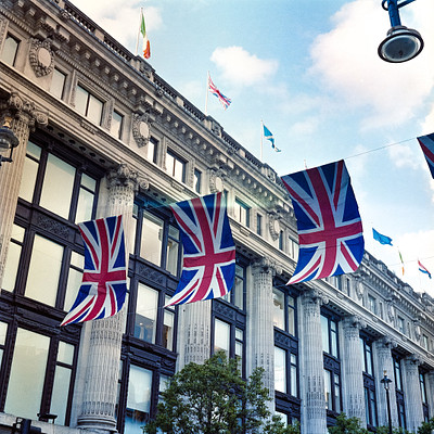 The image features a large building with many windows, including some on the top floor. There are several flags flying in front of the building, creating an impressive display. In total, there are 13 flags visible, each varying in size and positioning.