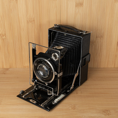 The image features an old-fashioned camera sitting on a wooden table. It is placed in the center of the scene, drawing attention to its vintage design. The camera appears to be black and silver, with a leather case surrounding it.