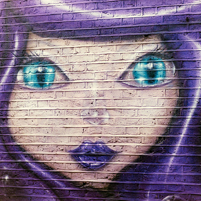 The image features a purple-haired girl with blue eyes, painted on the side of a brick wall. She appears to be looking directly at the viewer, capturing their attention. The painting is quite detailed and vibrant, showcasing the artist's skill in creating an eye-catching piece of artwork.