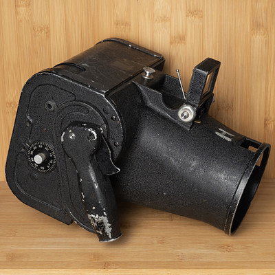 The image features a black camera with a wooden background. The camera is placed on a table, and it appears to be an old-fashioned model. There are several screws visible in the camera, indicating that it may have been disassembled for maintenance or repair purposes.