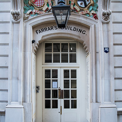 The image features a white building with an ornate doorway, which has a sign on it that reads "Farrars' Building." Above the doorway is a lamp post, adding to the architectural details of the entrance. Inside the building, there are several potted plants placed throughout the space, creating a welcoming atmosphere. The combination of the ornate doorway and the presence of potted plants gives the impression that this might be an old or historic building.