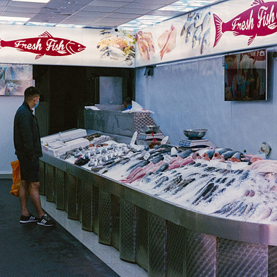 The image is a black and white photo of a fish market with a man standing in front of it. There are several fish displayed on the counter, including various types of fish such as salmon and tuna. A large bowl can be seen placed near the center of the counter.