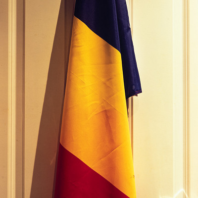 The image features a red, white, and blue flag hanging on the wall. It is positioned in front of a doorway, with the door visible behind it. The flag appears to be waving slightly, adding movement to the scene.