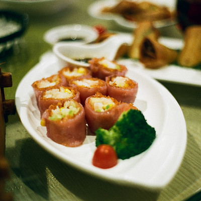 The image features a dining table with various plates of food, including sushi rolls and vegetables. There are several bowls on the table, one containing broccoli and another holding carrots. A white plate is filled with different types of sushi rolls, showcasing an appetizing assortment of dishes.