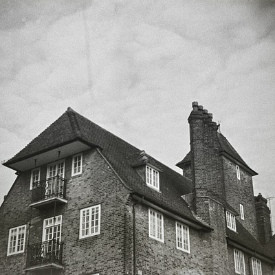 The image is a black and white photo of two brick buildings with steep roofs. One building has a chimney on top, while the other does not. Both buildings have many windows, giving them an old-fashioned appearance.