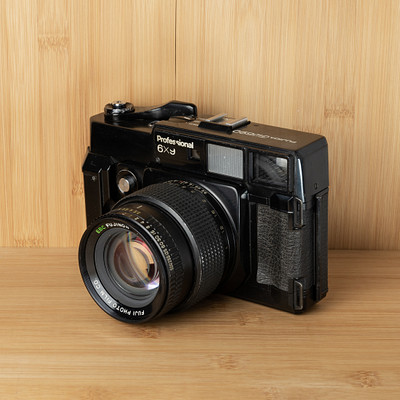 The image features an old-fashioned black and white camera sitting on a wooden table. The camera is placed in the center of the scene, with its lens facing towards the viewer. The wooden surface provides a natural backdrop for this vintage piece of photography equipment.