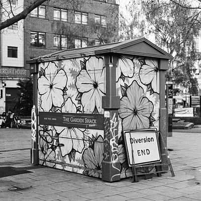 The image is a black and white photo of a public restroom in an urban setting. The restroom features a unique design with butterfly patterns on the walls, giving it a creative touch. There are several benches placed around the area for people to sit while using the facilities.