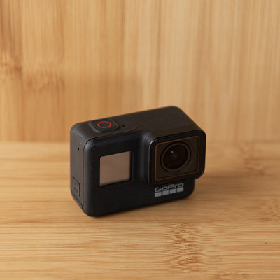 The image features a small black camera sitting on top of a wooden table. The camera is positioned in the center of the scene, with its lens facing upwards. The wooden surface provides an appealing backdrop for this compact device.