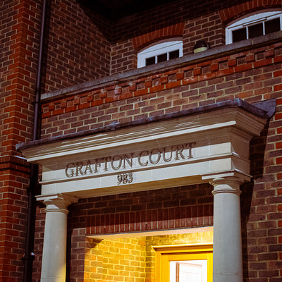 The image features a large brick building with an arched entrance, which has the words "GRAFTON COURT" written on it. The doorway is open and inviting, leading to the interior of the building. The architecture of the building appears to be old-fashioned, giving it a historical feel.