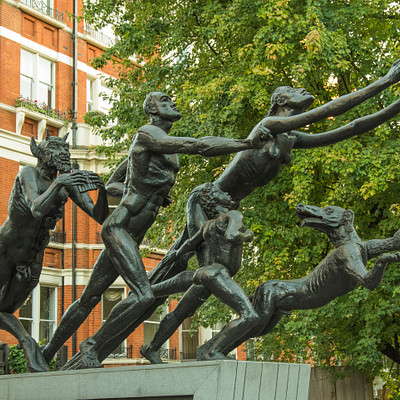 The image features a group of statues, including men and women, arranged in various poses. They are all standing on top of a cement platform or pedestal. Some of the statues appear to be interacting with each other, creating an interesting scene.