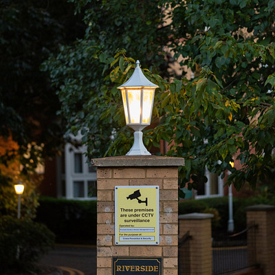 The image features a street sign with a light on top of it, located in front of a brick building. The sign is surrounded by a fence and has a private property sign underneath it. There are also two signs posted below the main sign, providing additional information or directions for passersby.
