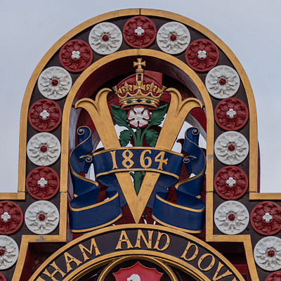 The image features a large, ornate wooden sign with a royal crown on top. The sign is decorated with red and blue colors, giving it an old-fashioned appearance. It appears to be located in the town of Wingham or Hampton, as indicated by the name on the sign.