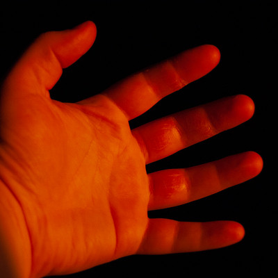 The image features a hand with red fingernails, reaching out towards the camera. The hand is positioned in front of a dark background, which creates an interesting contrast between the hand and its surroundings.
